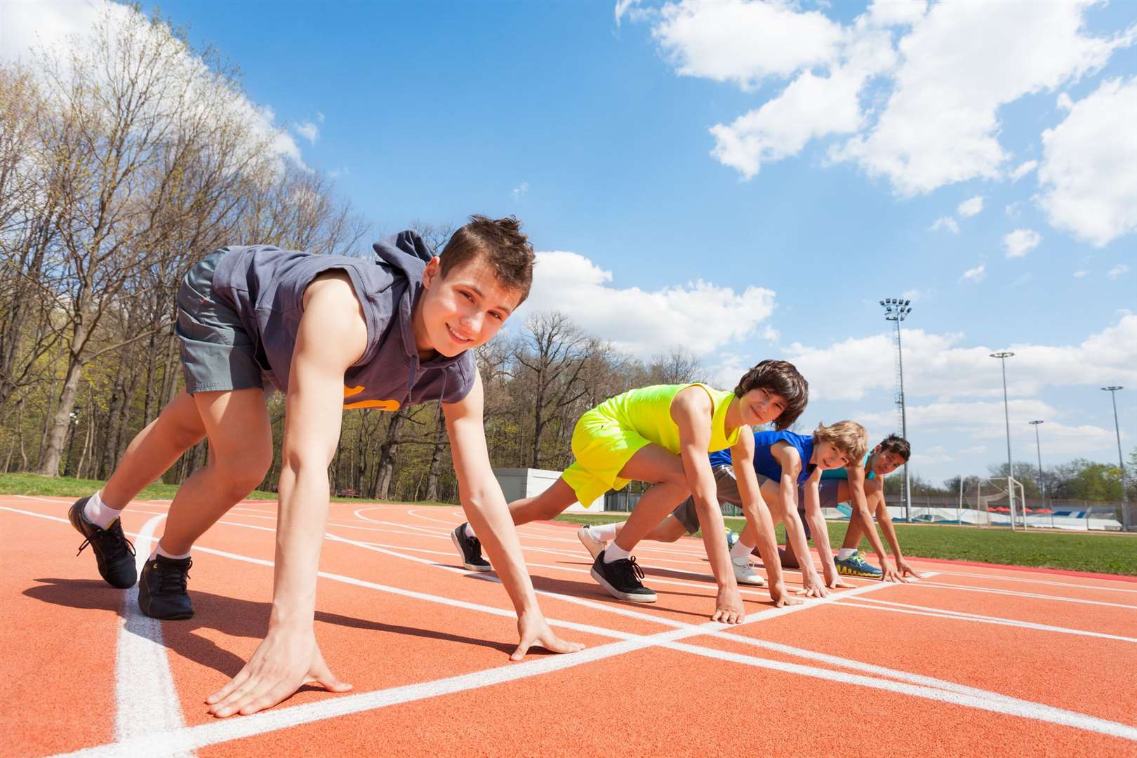 Side view of four teenage boys in sportswear lined up ready to race at the stadium. (45272399)